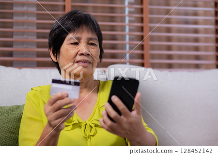 Senior asian woman sitting on sofa using smart phone shopping online with credit card. 128452142