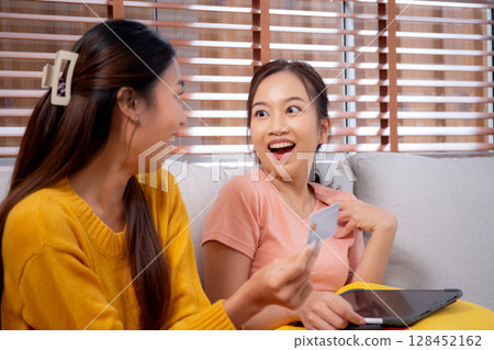 Two young asian woman sitting on sofa using tablet computer shopping online with credit card. Two young asian woman sitting on sofa using tablet computer shopping online with credit card. 128452162