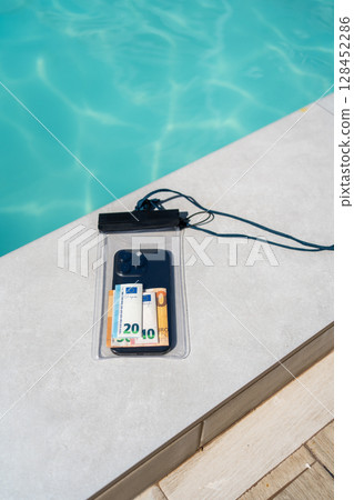 Waterproof case with money and a smartphone on the background of the pool on a sunny summer day Waterproof case with money and a smartphone on the background of the pool on a sunny summer day 128452286
