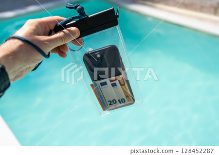 Waterproof case with money and a smartphone on the background of the pool on a sunny summer day Waterproof case with money and a smartphone on the background of the pool on a sunny summer day 128452287