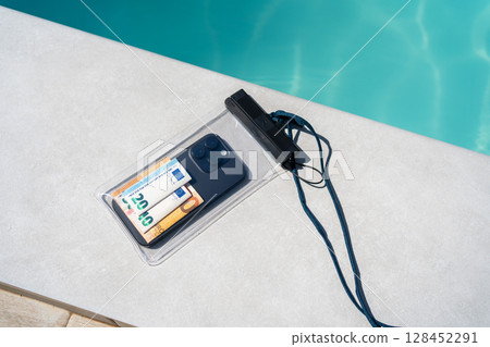 Waterproof case with money and a smartphone on the background of the pool on a sunny summer day 128452291