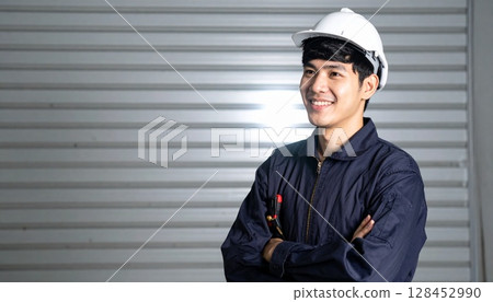 A smiling man wearing work clothes and a helmet with his arms folded 128452990