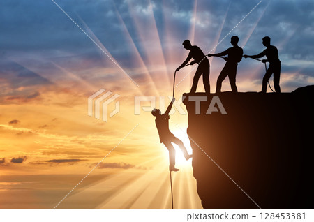 Silhouette of three climbers pulling out of the cliff of a man. Silhouette of three climbers pulling out of the cliff of a man. 128453381