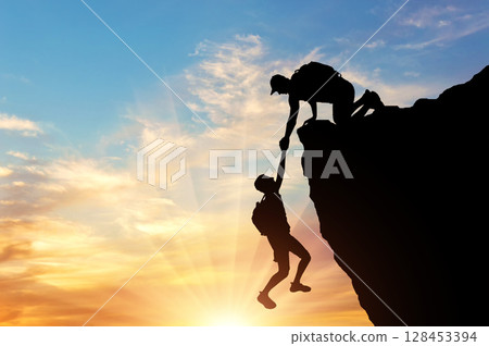Silhouette of a climber saves another climber pulling him from the abyss Silhouette of a climber saves another climber pulling him from the abyss 128453394