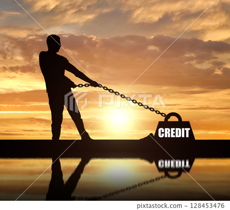 Silhouette of a man chained to a heavy load under the name of the credit. He drags him hard. 128453476