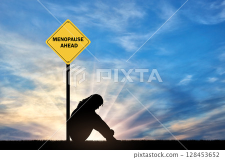 Sad woman sitting in front of a road sign menopause ahead. 128453652