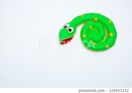 Soft toy small green striped smiling snake isolated on white background. The concept of wisdom and humor Soft toy small green striped smiling snake isolated on white background. The concept of wisdom and humor 128455232