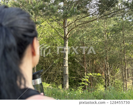 Athletic brunette woman in sportswear holding shaker and water bottle during outdoor workout in forest. Fitness lifestyle, hydration, active living, healthy recreation in nature 128455730