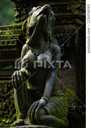 Monkey sculpture fully covered with green moss in Ubud's Monkey Forest. Bali, Indonesia. 128456045