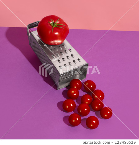 Whole tomato resting on grater with cherry tomatoes scattered on purple surface 128456529
