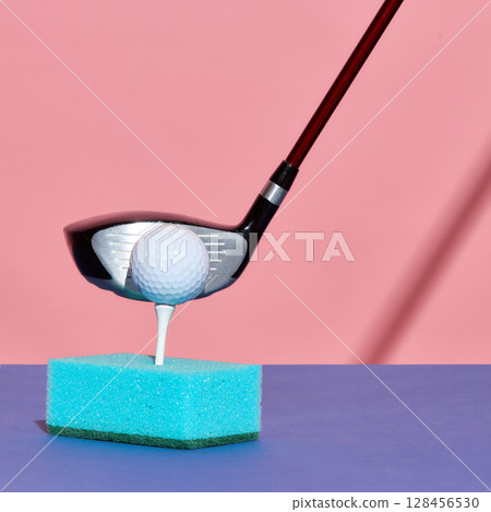 Golf club about to strike ball positioned on tee inserted in blue kitchen sponge Golf club about to strike ball positioned on tee inserted in blue kitchen sponge 128456530