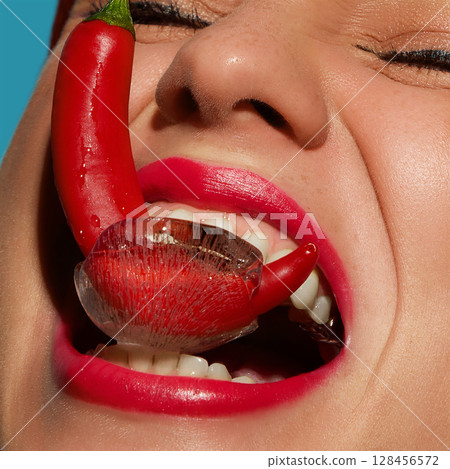 Laughing woman biting chili pepper frozen in ice with playful facial expression Laughing woman biting chili pepper frozen in ice with playful facial expression 128456572