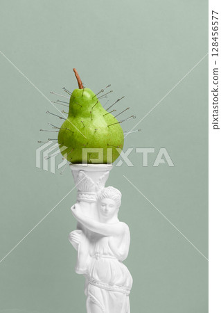 Closeup green pear with safety pins on neoclassical statue against soft green backdrop 128456577