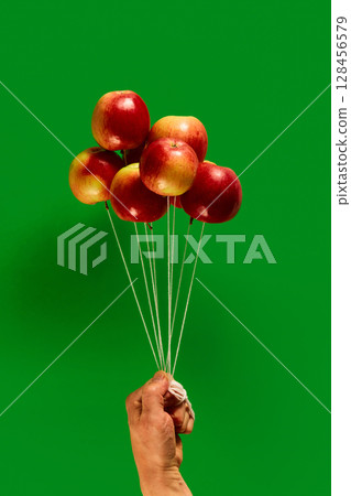 Red apples tied like balloons and held in human hand on green background Red apples tied like balloons and held in human hand on green background 128456579