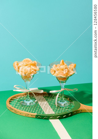 Tangerine wedges in glasses on vintage tennis racket over green and blue pastel background 128456580