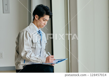 一個穿著工作服的年輕人在檢查某件東西 一個穿著工作服的年輕人在檢查某件東西 128457014