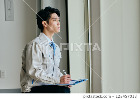 A young man in work clothes inspecting something A young man in work clothes inspecting something 128457018
