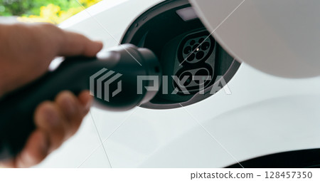 Hand holding EV charger near electric car socket Hand holding EV charger near electric car socket 128457350