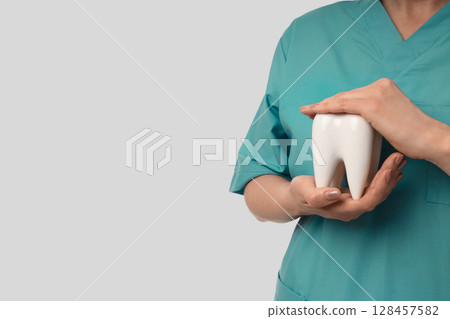 A person in scrubs is holding a large tooth model carefully 128457582