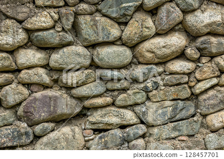 Rustic stone wall made with various sizes and shapes of round rocks 128457701