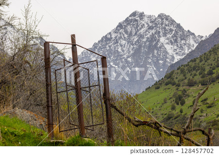 Rusty chain link fence with rotating wicket in mountains of Kyrgyzstan 128457702