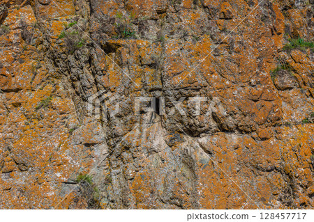 Rugged rock formation with orange lichen and crevice outdoors Rugged rock formation with orange lichen and crevice outdoors 128457717