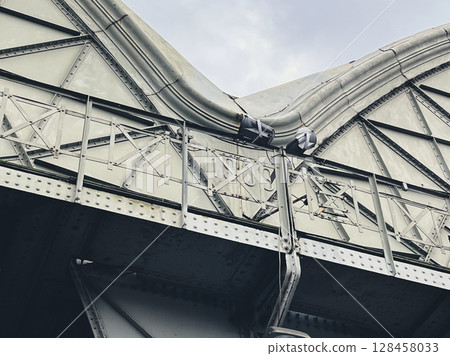 Close-up of a metal bridge structure against a cloudy sky. 128458033
