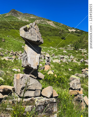 Stone cairns on a green hillside against blue sky. Stone cairns on a green hillside against blue sky. 128458055