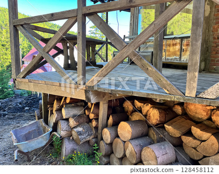 Rustic wooden cabin porch with stacked firewood in a serene landscape. Rustic wooden cabin porch with stacked firewood in a serene landscape. 128458112