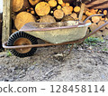Old wheelbarrow and firewood pile in a rustic outdoor setting. 128458114