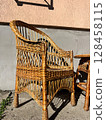 Wicker chair and table in sunlight against a wall background. 128458115