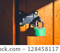 Green padlock on wooden door in sunlight conveying security. 128458117