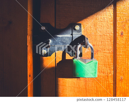 Green padlock on wooden door in sunlight conveying security. Green padlock on wooden door in sunlight conveying security. 128458117