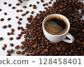 Coffee cup surrounded by roasted beans on white surface. 128458401