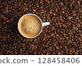 White coffee cup with froth placed on roasted beans, close-up from above. 128458406