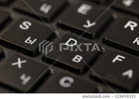 black keyboard with English and Russian letters close up, the keyboard in the layout of letters in several languages black keyboard with English and Russian letters close up, the keyboard in the layout of letters in several languages 128459335