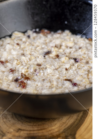 porridge with dried fruits in a black bowl , cooking instant oatmeal porridge, close up, side view 128459370