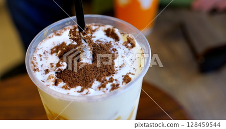Skilled barista sprinkling cocoa powder over whipped cream, creating artistic latte design with precise dark straw garnishing technique Skilled barista sprinkling cocoa powder over whipped cream, creating artistic latte design with precise dark straw garnishing technique 128459544