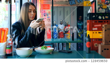 Young female food blogger capturing vibrant meal using smartphone while sitting in colorful asian restaurant, showcasing digital lifestyle and culinary culture through social media content creation 128459650