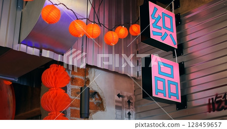 Pink neon sign with chinese characters hanging from the ceiling of a restaurant, illuminated by purple light, with a string of orange paper lanterns and red decorations hanging nearby Pink neon sign with chinese characters hanging from the ceiling of a restaurant, illuminated by purple light, with a string of orange paper lanterns and red decorations hanging nearby 128459657