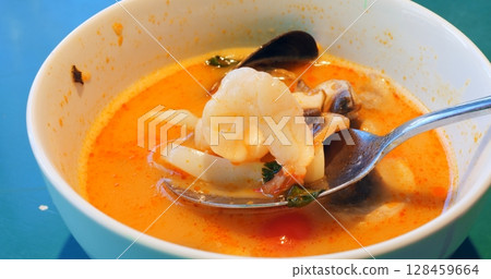 Discovering savory tom yam soup delicacy with metallic spoon, carefully extracting succulent shrimps, tender mushrooms, ripe tomatoes, fresh fish, aromatic herbs from vibrant broth Discovering savory tom yam soup delicacy with metallic spoon, carefully extracting succulent shrimps, tender mushrooms, ripe tomatoes, fresh fish, aromatic herbs from vibrant broth 128459664