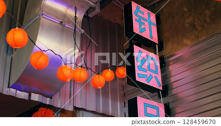 Pink neon signs with chinese characters and a string of red paper lanterns decorate the exterior of a building, adding a vibrant touch to the facade with restroom signs in the background 128459670