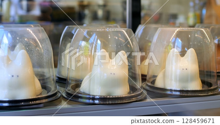 Delicious mousse cakes shaped like white rabbits and chocolate cupcakes inside plastic containers, are displayed on metal shelves of a refrigerated display case in a bakery or pastry shop Delicious mousse cakes shaped like white rabbits and chocolate cupcakes inside plastic containers, are displayed on metal shelves of a refrigerated display case in a bakery or pastry shop 128459671