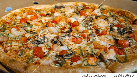 Round pizza with shrimps, tomatoes, mushrooms, and pesto rotates slightly on a cardboard box, showcasing its delicious toppings and crispy crust Round pizza with shrimps, tomatoes, mushrooms, and pesto rotates slightly on a cardboard box, showcasing its delicious toppings and crispy crust 128459680