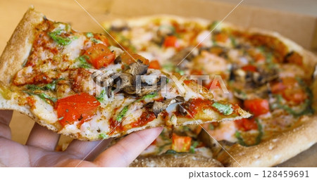 Professional chef hands presenting appetizing pizza slice, layered with succulent shrimps, ripe tomatoes, savory mushrooms, and melted cheese against pristine white background 128459691