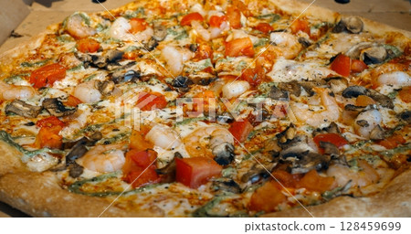 Round pizza with shrimps, mushrooms, tomatoes, and mozzarella cheese rotates slowly on a cardboard base, creating a tempting culinary display Round pizza with shrimps, mushrooms, tomatoes, and mozzarella cheese rotates slowly on a cardboard base, creating a tempting culinary display 128459699