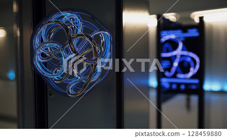 Intricate metallic wires intertwining and glowing with blue and gold light, creating a mesmerizing visual display in a modern interior with digital signage in the background 128459880