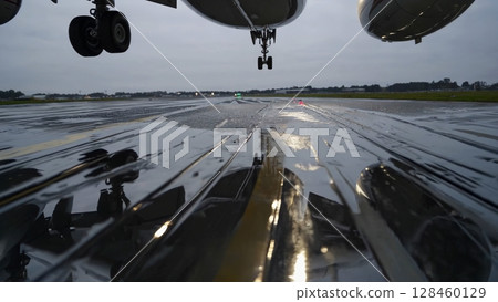 Passenger airplane smoothly taxiing on glistening wet runway, sunlight reflecting across rain soaked airport surface, capturing dramatic aviation moment 128460129
