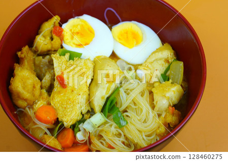 A vibrant bowl of Bihun Kari or Indonesian curry vermicelli noodles, chicken, eggs, and vegetables in a rich yellow broth. 128460275