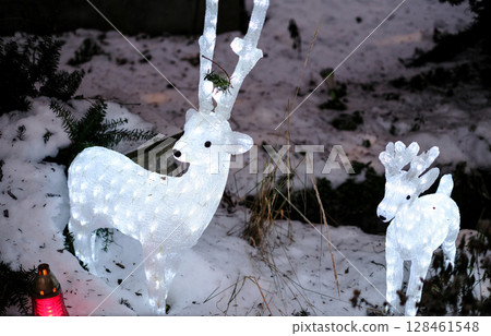Striking outdoor Christmas decoration featuring two illuminated white reindeer figures standing in fresh snow 128461548